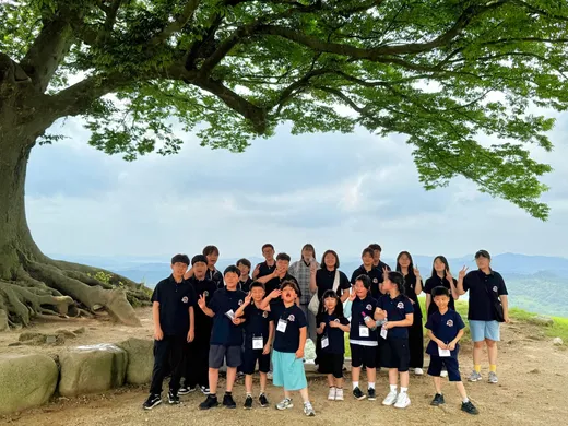 언덕 위 큰 나무 아래 모인 오하비 학생과 선생님들